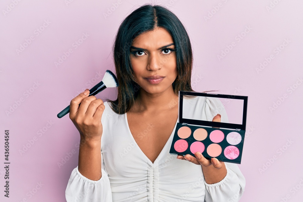 Young latin transsexual transgender woman holding makeup brush and blush palette skeptic and nervous, frowning upset because of problem. negative person. Young latin transsexual transgender woman holding makeup brush and blush palette skeptic and nervous, frowning upset because of problem. negative person.