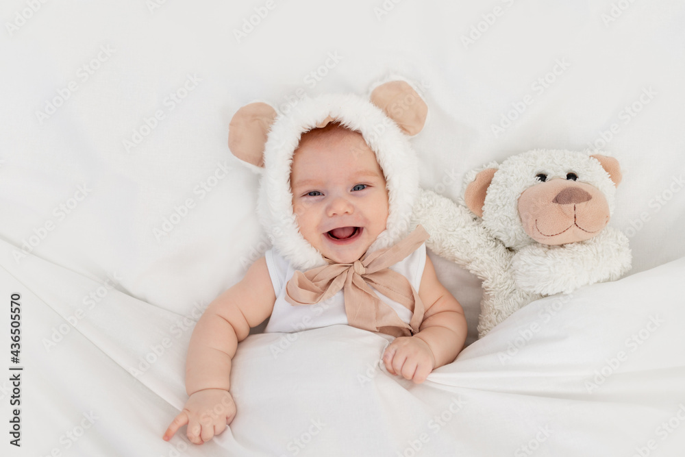 a child in a funny hat with ears with a teddy bear under the blanket. Textiles and bed linen for children. A newborn baby has woken up or is going to bed a child in a funny hat with ears with a teddy bear under the blanket. Textiles and bed linen for children. A newborn baby has woken up or is going to bed