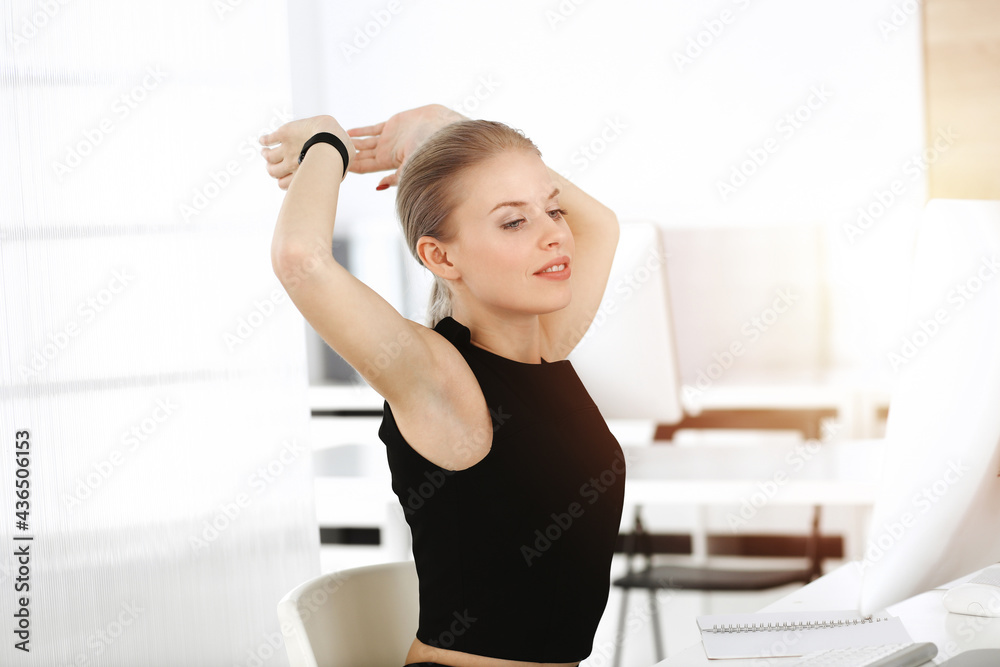Young blond businesswoman dressed in black dress looks perfect in sunny modern office. Business people concept Young blond businesswoman dressed in black dress looks perfect in sunny modern office. Business people concept