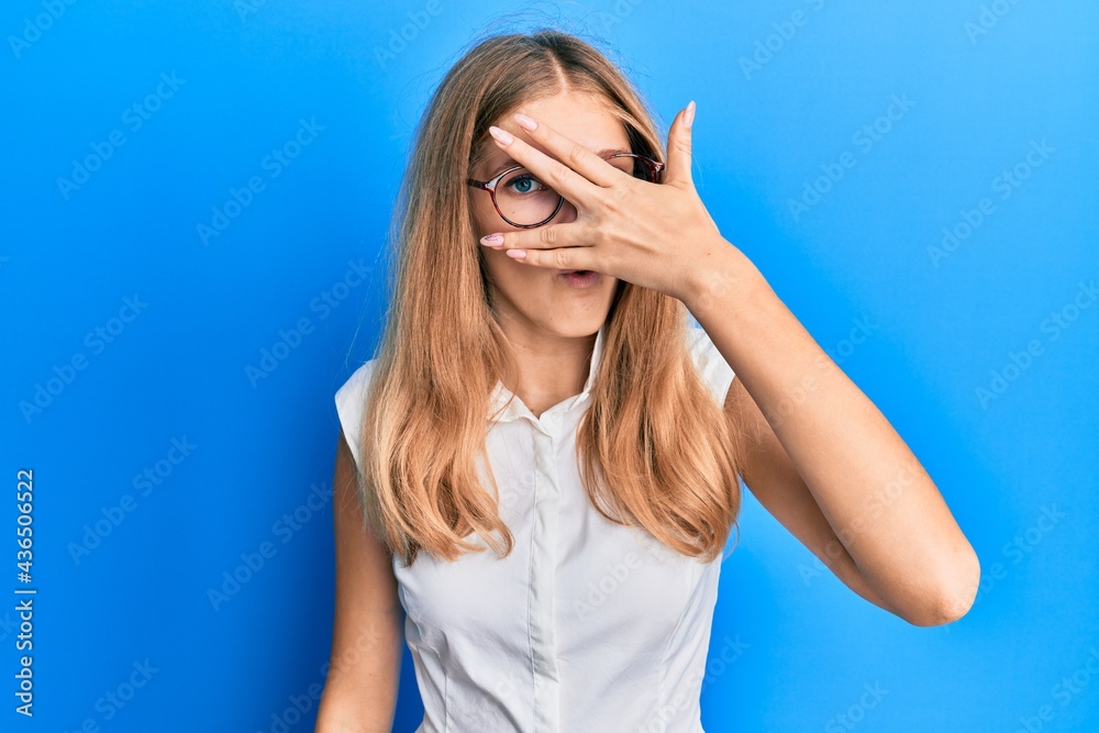 Beautiful young caucasian girl wearing casual clothes and glasses peeking in shock covering face and eyes with hand, looking through fingers afraid