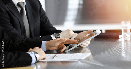 Businessman using tablet computer and work together with his colleague in sunny modern office, close-up. Unknown business people at meeting. Teamwork and partnership concept