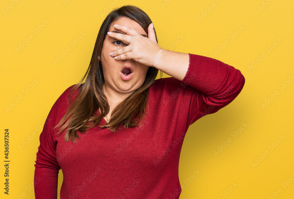 Beautiful brunette plus size woman wearing casual clothes peeking in shock covering face and eyes with hand, looking through fingers with embarrassed expression.