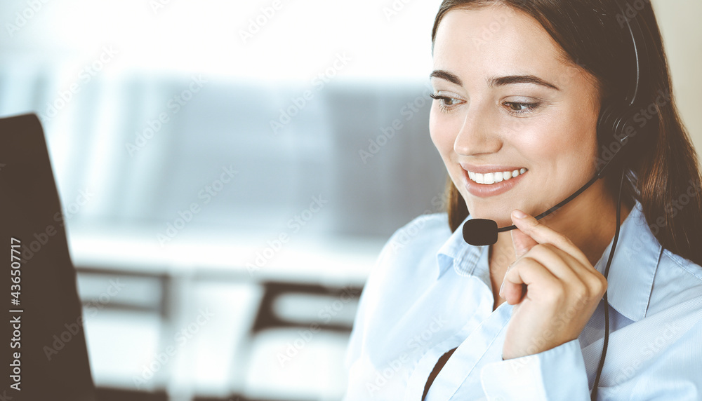 Brunette female customer service representative in a headset is consulting clients online. Call center and business people concept Brunette female customer service representative in a headset is consulting clients online. Call center and business people concept