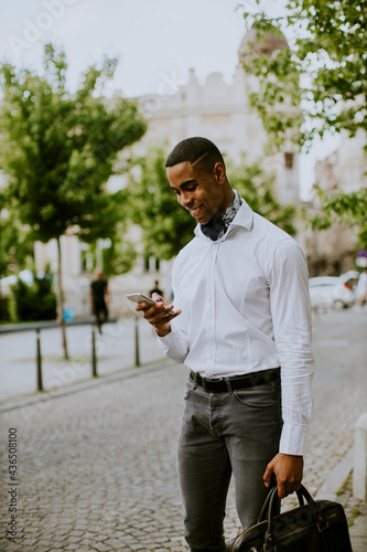 Young African American businessman using a mobile phone while waitng for a taxi on a street photo