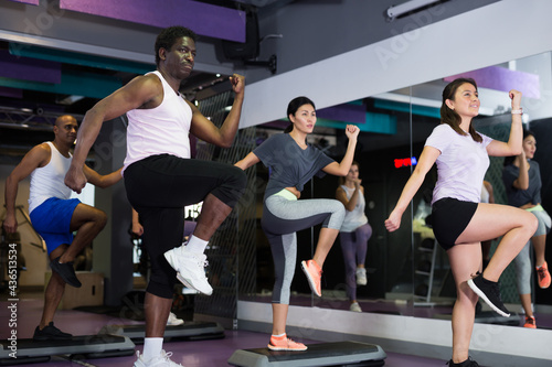 Athletic people performing step aerobics in fitness club