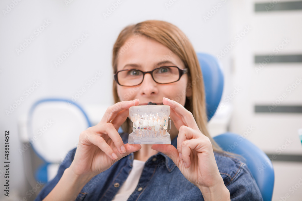Female patient holding dental model with braces, waiting for medical exam at the dentist Female patient holding dental model with braces, waiting for medical exam at the dentist