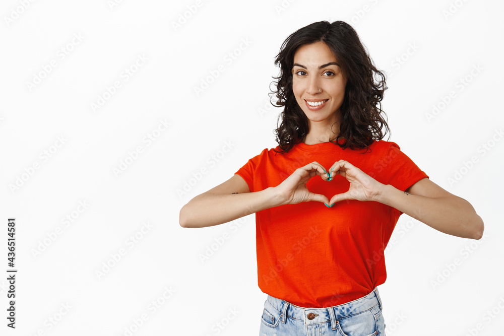 Lovely brunette woman shows heart sign, smiling and looking heartwarming, express love and tenderness, likes you, white background Lovely brunette woman shows heart sign, smiling and looking heartwarming, express love and tenderness, likes you, white background