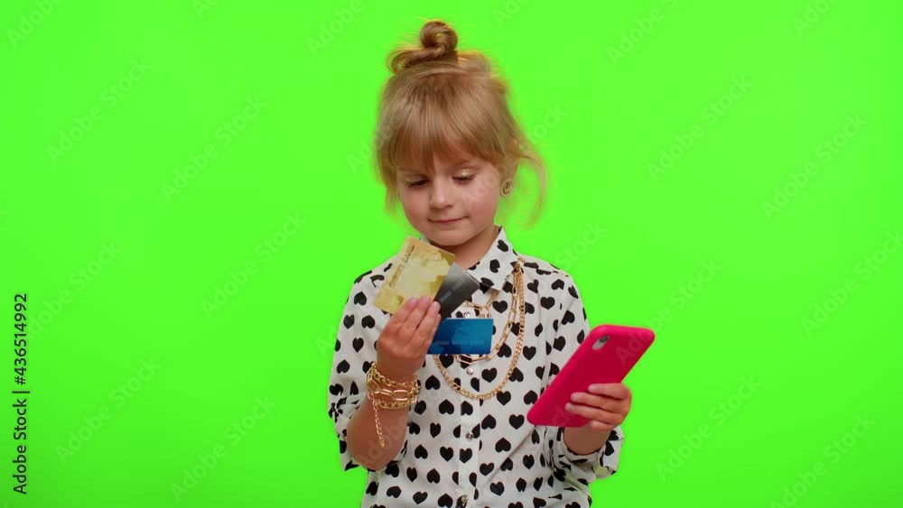 Little blonde teen kid child girl using plastic credit bank cards and smartphone while transferring money purchases online shopping. Young children with mobile phone posing on chroma key background Little blonde teen kid child girl using plastic credit bank cards and smartphone while transferring money purchases online shopping. Young children with mobile phone posing on chroma key background