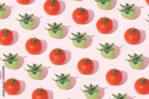 A pattern of green and red tomatoes with a stalk on a pink background. Minimal vegetablest flat lay