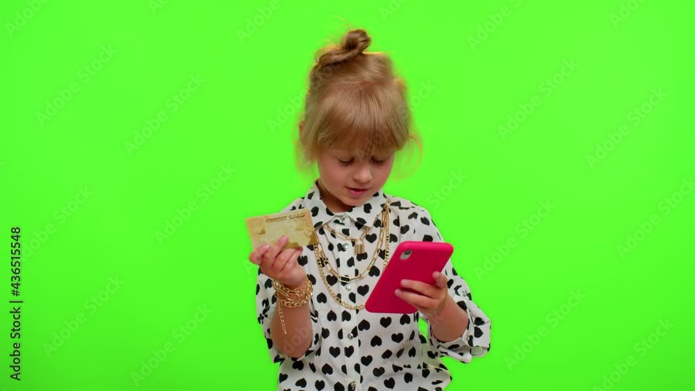 Little blonde teen kid child girl using plastic credit bank card and smartphone while transferring money, purchases online shopping. Young children with mobile phone posing on chroma key background Little blonde teen kid child girl using plastic credit bank card and smartphone while transferring money, purchases online shopping. Young children with mobile phone posing on chroma key background
