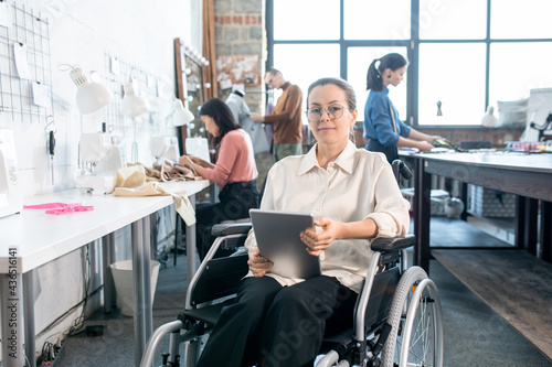 Young successful fashion designer in wheelchair using tablet in working environment