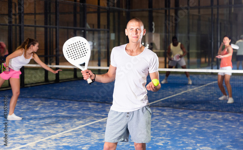 Portrait of smiling sporty male in white t-shirt with padel racket at court © JackF