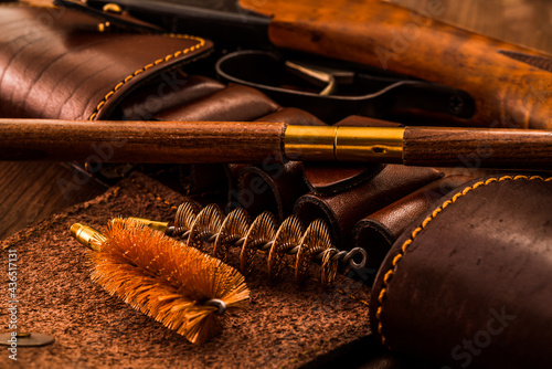 Hunting rifle with leather bandolier and a ramrod with brushes for cleaning weapons lying on a wooden table