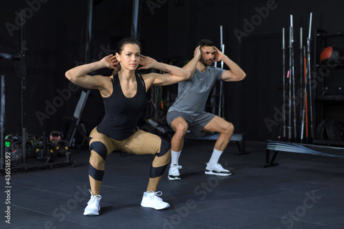 Fototapeta Naklejka Na Ścianę i Meble -  Fitness couple in sportswear doing squat exercises at gym.