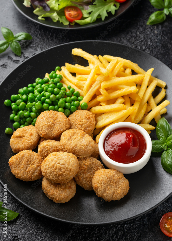 Fried crispy chicken nuggets with ketchup, french fries and green peas in black plate Fried crispy chicken nuggets with ketchup, french fries and green peas in black plate