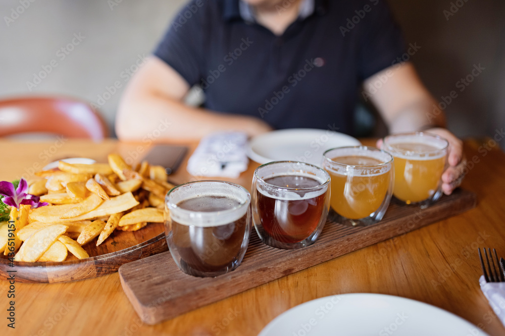 Man sampling variety of seasonal craft beer in pub. Beer samplers in small glasses individually placed in holes fashioned into unique wooden tray. Selective focus with shallow depth of field. Man sampling variety of seasonal craft beer in pub. Beer samplers in small glasses individually placed in holes fashioned into unique wooden tray. Selective focus with shallow depth of field.