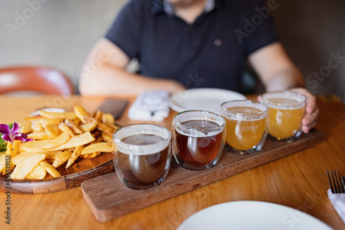 Man sampling variety of seasonal craft beer in pub. Beer samplers in small glasses individually placed in holes fashioned into unique wooden tray. Selective focus with shallow depth of field.