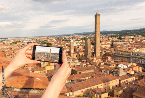 travel concept - tourist takes picture of Due Torri -two tower - symbol of city in Bologna, Italy on smartphone photo