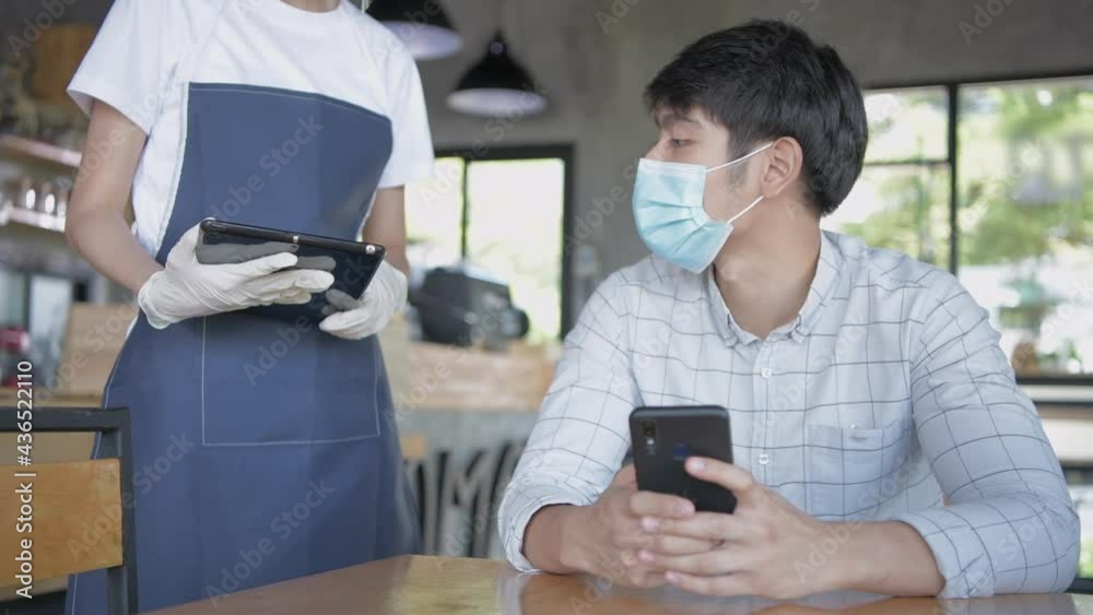 Coffee shop concept of 4k Resolution. A young Asian man is paying by mobile phone with a waiter. Coffee shop concept of 4k Resolution. A young Asian man is paying by mobile phone with a waiter.
