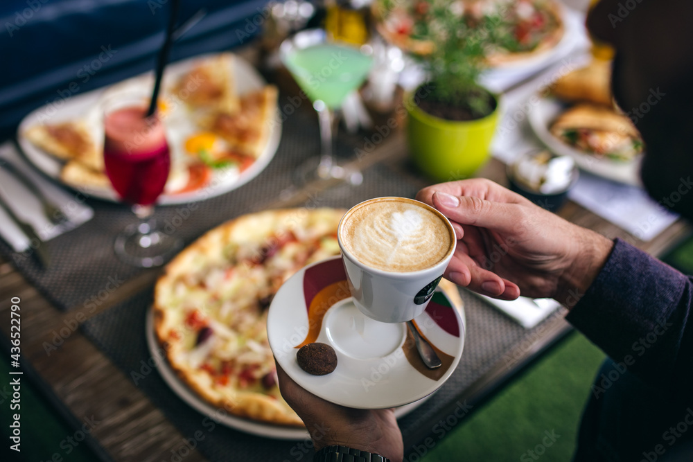 man holding cup of coffee in front of pizza in restaurant