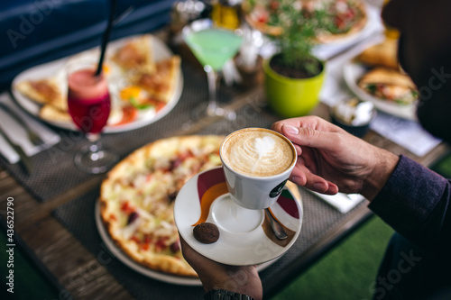 man holding cup of coffee in front of pizza in restaurant