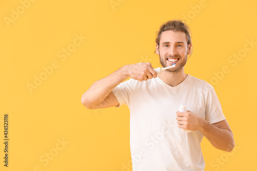 Young man brushing teeth on color background