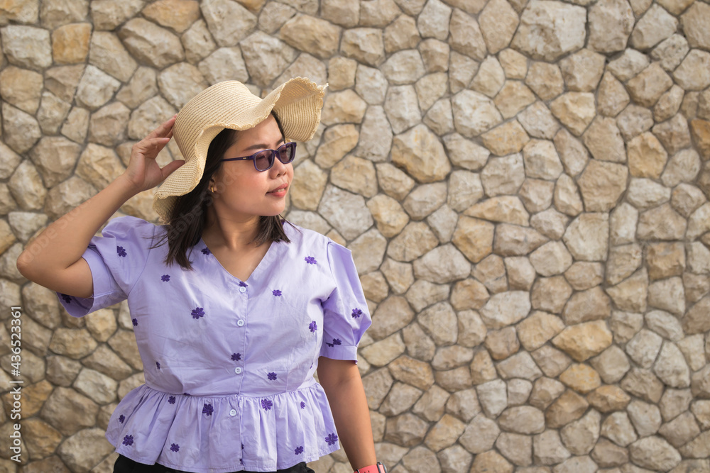 Asian woman dressed in purple shirt wearing glasses and straw hat on brick wall background. Asian woman dressed in purple shirt wearing glasses and straw hat on brick wall background.
