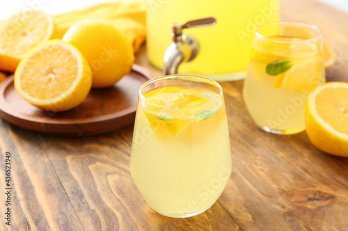 Jar and glasses of tasty cold lemonade on wooden background