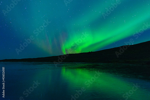 Northern Lights on the night sky. Wintertime starry sky. Aurora Borealis above a frozen lake.