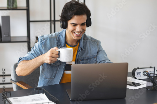 Young caucasian man sitting at the table at home with laptop looking at the camera and smiling pleasantly, online education or training