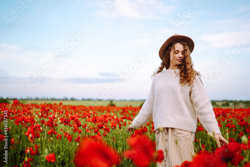 Young woman walking in amazing poppy field. Summertime. Beautiful woman posing in the blooming poppy field. Nature, vacation, relax and lifestyle.