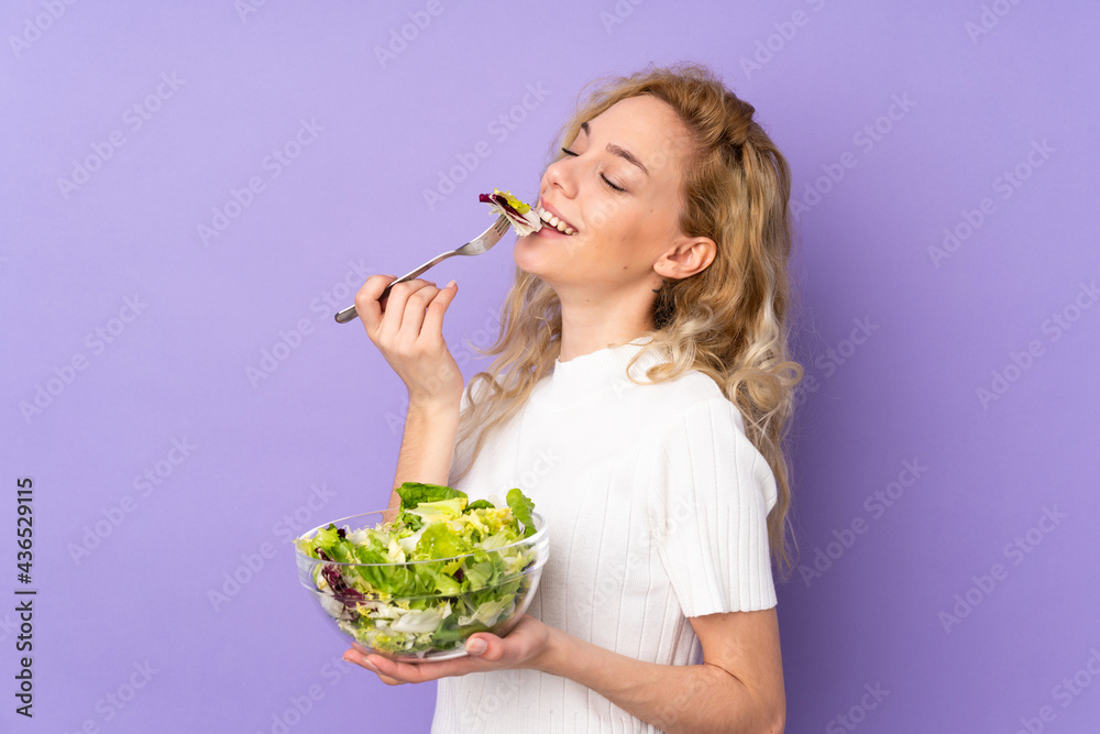 Young blonde woman holding salad isolated on purple background