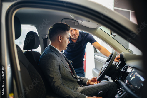 A young businessman with a salesman looks at a new car in a car dealership. Buying a car © Andrii