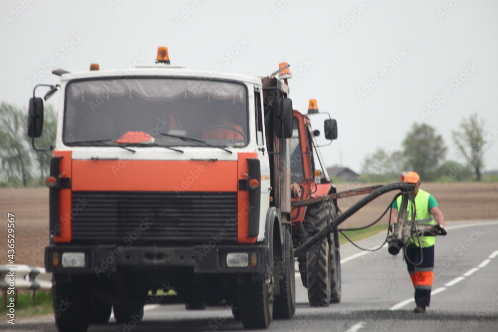 Highway road repair local holes with Bitumen, asphalt machine truck and one road worker elderly man in hard hat and coveralls at summer day, road building industrial machines and heavy job Highway road repair local holes with Bitumen, asphalt machine truck and one road worker elderly man in hard hat and coveralls at summer day, road building industrial machines and heavy job