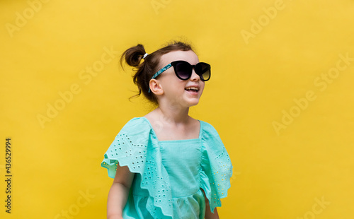 a cute little girl in sunglasses looks away on a yellow background with a copy of the space. Sunscreen accessories for children