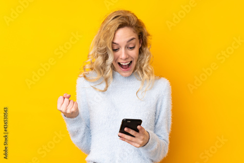 Young blonde woman isolated on yellow background surprised and sending a message