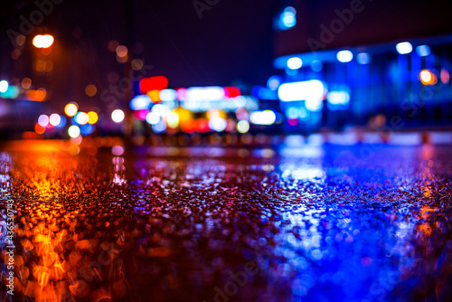 Rainy night in the big city, road in the light of shop windows. View from the level of asphalt