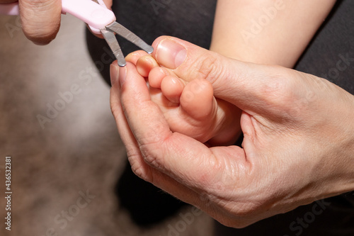 Mom s hand holding little scissors to cut nails on tiny baby   s foot.