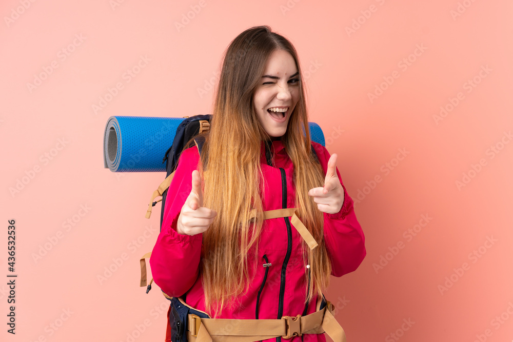 Young mountaineer girl with a big backpack isolated on pink background points finger at you Young mountaineer girl with a big backpack isolated on pink background points finger at you