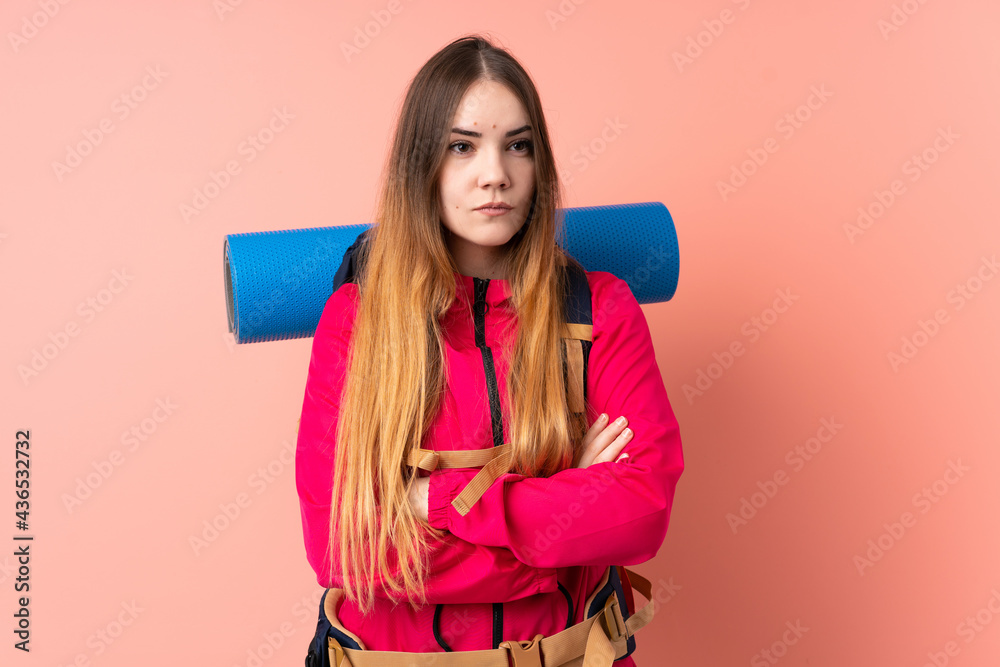 Young mountaineer girl with a big backpack isolated on pink background keeping arms crossed Young mountaineer girl with a big backpack isolated on pink background keeping arms crossed