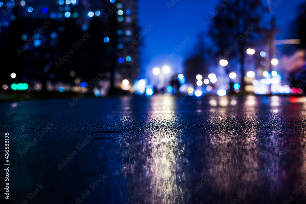 Rainy night in the big city, alley in the city park with walking people. View from the level of asphalt