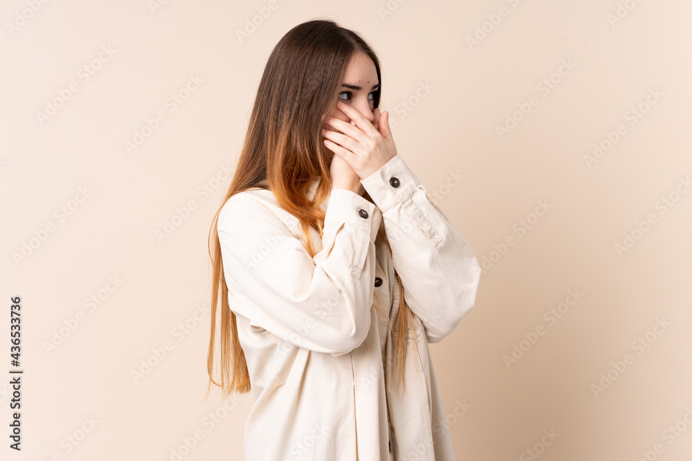 Young caucasian woman isolated on beige background covering mouth and looking to the side Young caucasian woman isolated on beige background covering mouth and looking to the side