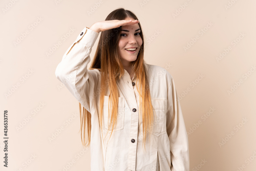 Young caucasian woman isolated on beige background looking far away with hand to look something Young caucasian woman isolated on beige background looking far away with hand to look something