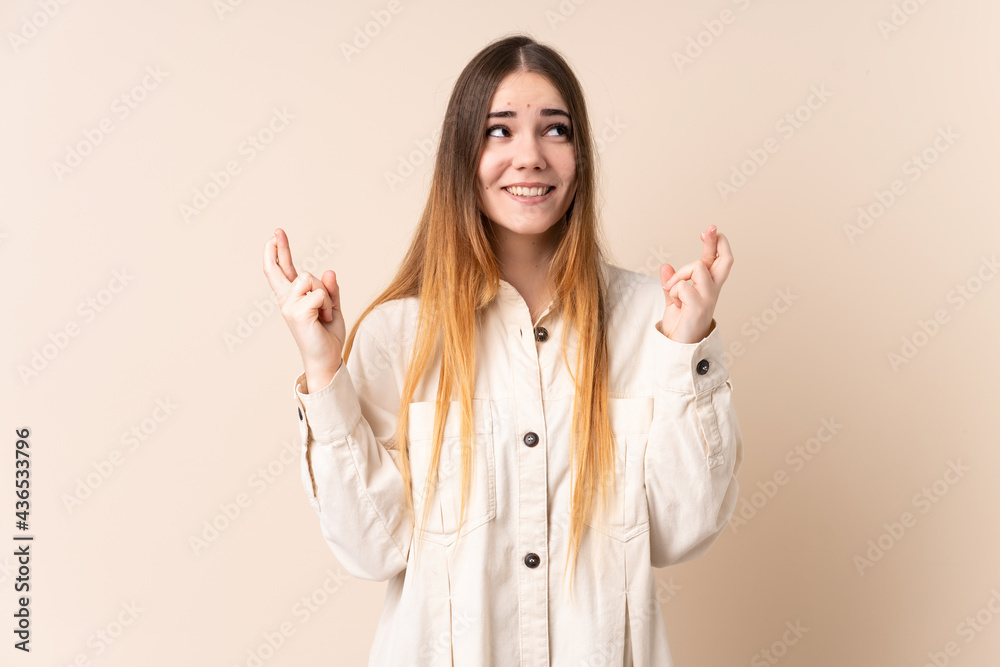 Young caucasian woman isolated on beige background with fingers crossing and wishing the best