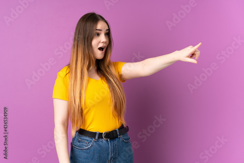 Young caucasian woman isolated on purple background pointing away
