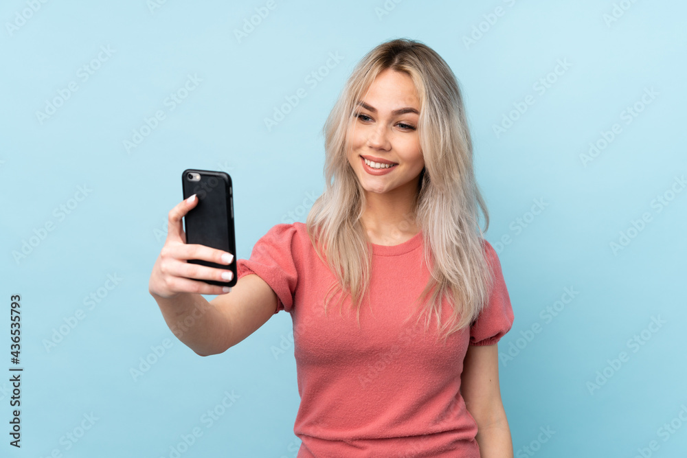 Teenager girl over isolated blue background making a selfie