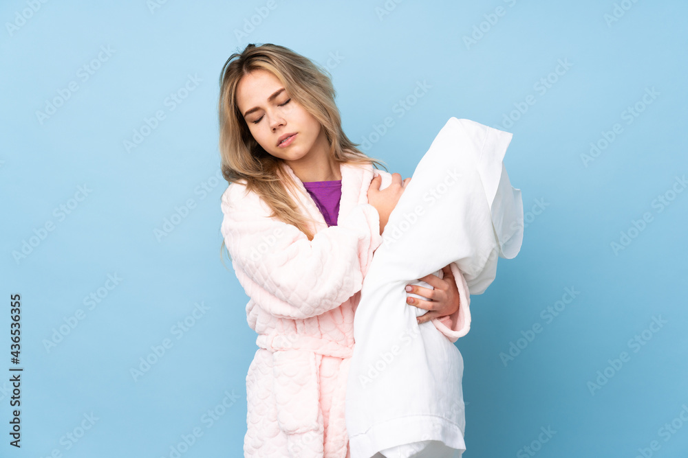 Teenager Russian girl in pajamas isolated on blue background suffering from pain in shoulder for having made an effort