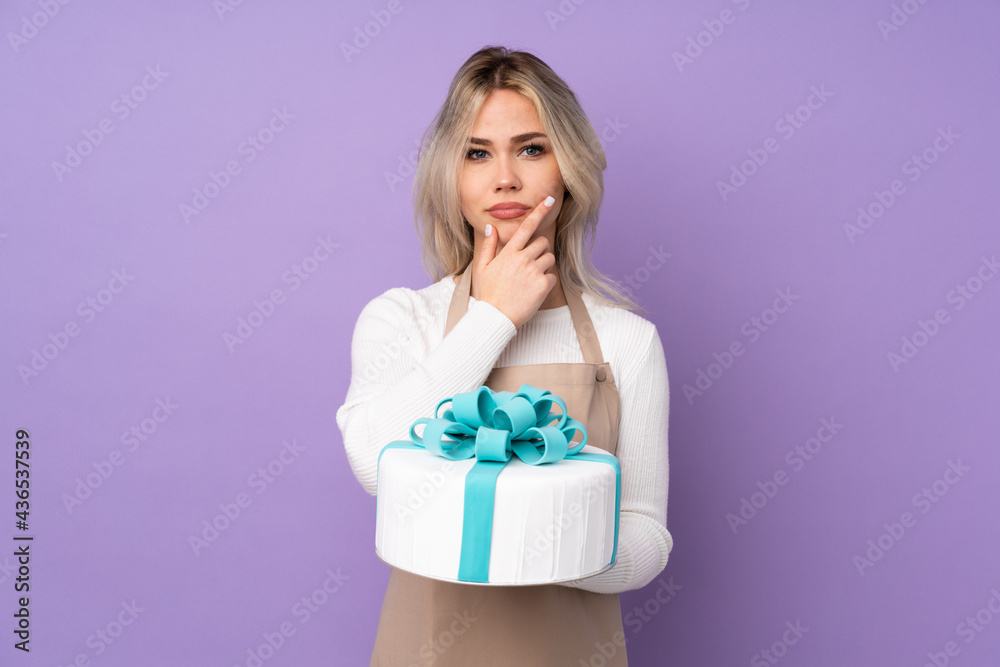 Young pastry chef holding a big cake over isolated purple background thinking an idea Young pastry chef holding a big cake over isolated purple background thinking an idea