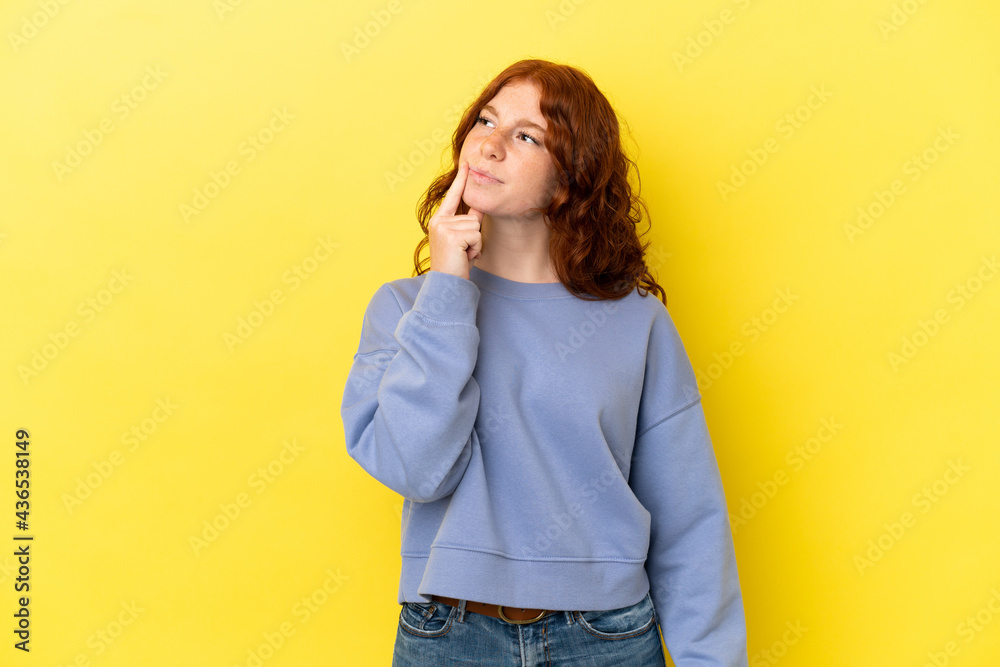 Teenager reddish woman isolated on yellow background having doubts while looking up Teenager reddish woman isolated on yellow background having doubts while looking up