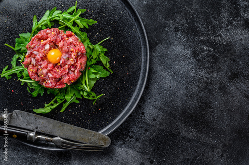 Beef tartar with a quail egg served on a black stone plate.. Black background. Top view. Copy space